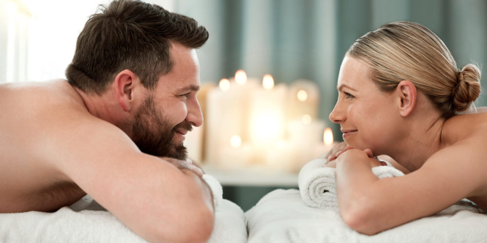 Couple, spa and luxury massage together for healthy, relax and wellness at a holiday resort. Happy man and woman in relationship looking at each other in massaging therapy for calm relaxation.